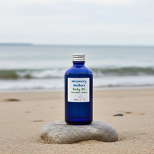 Load image into Gallery viewer, Blue bottle of Naturally Matters Body Oil on a rock with a beach background